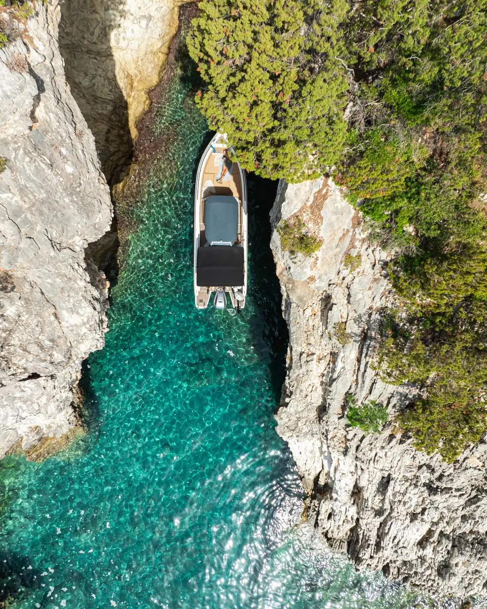 Drone photo of a small boat in a narrow turquoise bay between white cliffs